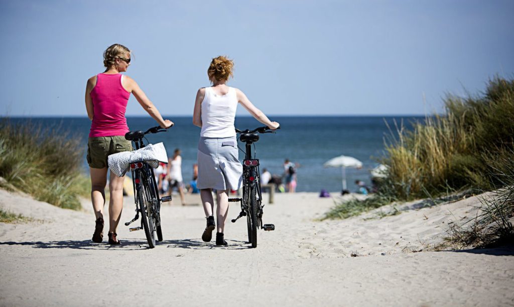 Zwei schöne Frauen, die mit ihren Fahrrädern am Marielyst-Strand auf Falster spazieren gehen